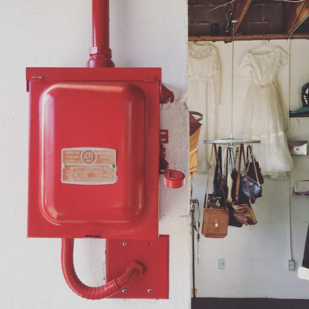 Red fire alarm box beside white dresses and handbag
