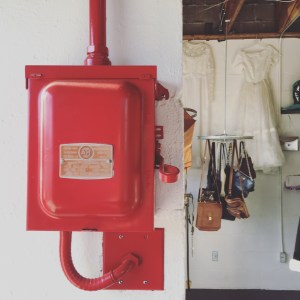 Red fire alarm box beside white dresses and handbag